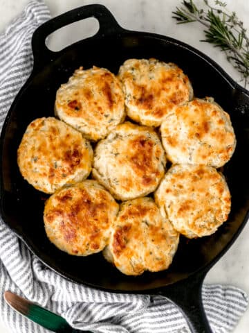 overhead view cheddar herb biscuits in cast iron skillet with napkin and fresh herbs