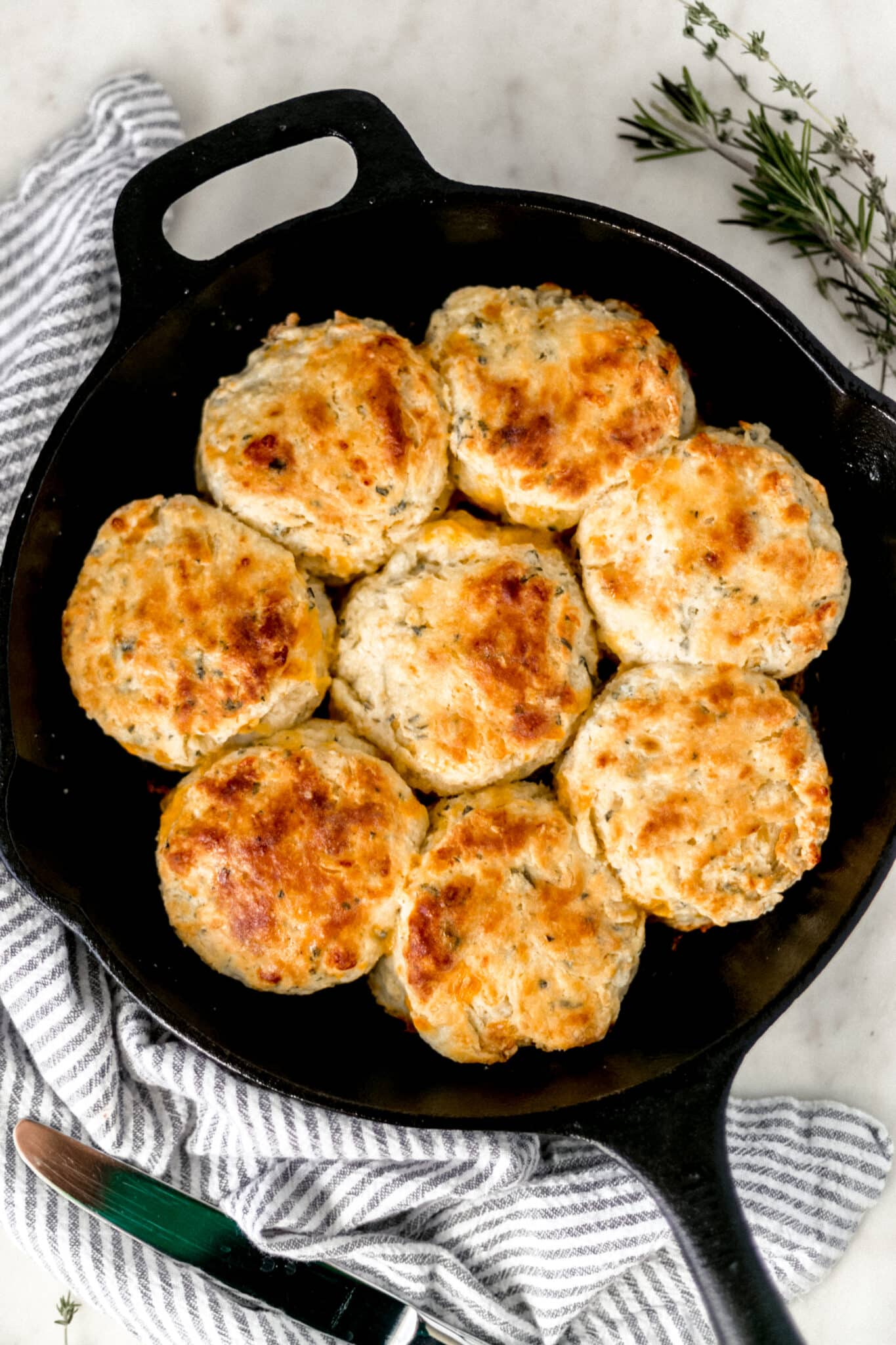 overhead view cheddar herb biscuits in cast iron skillet with napkin and fresh herbs