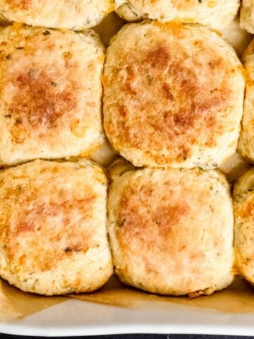 Overhead view of biscuits in white parchment lined baking dish on black tile surface.