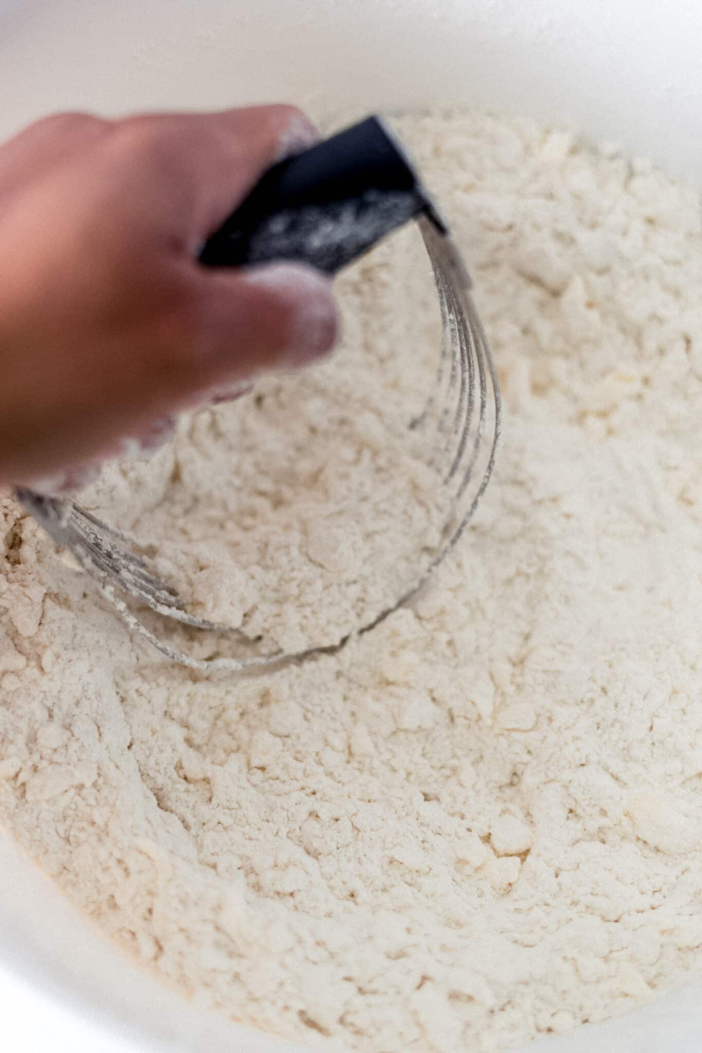 hand using pastry cutter to blend butter into dry ingredients in large bowl