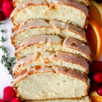 Close up view of sliced cake with fruit and herbs around it.
