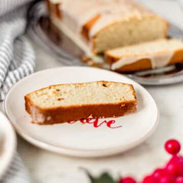 side view of slice of eggnog pound cake on plate with full cake in the background