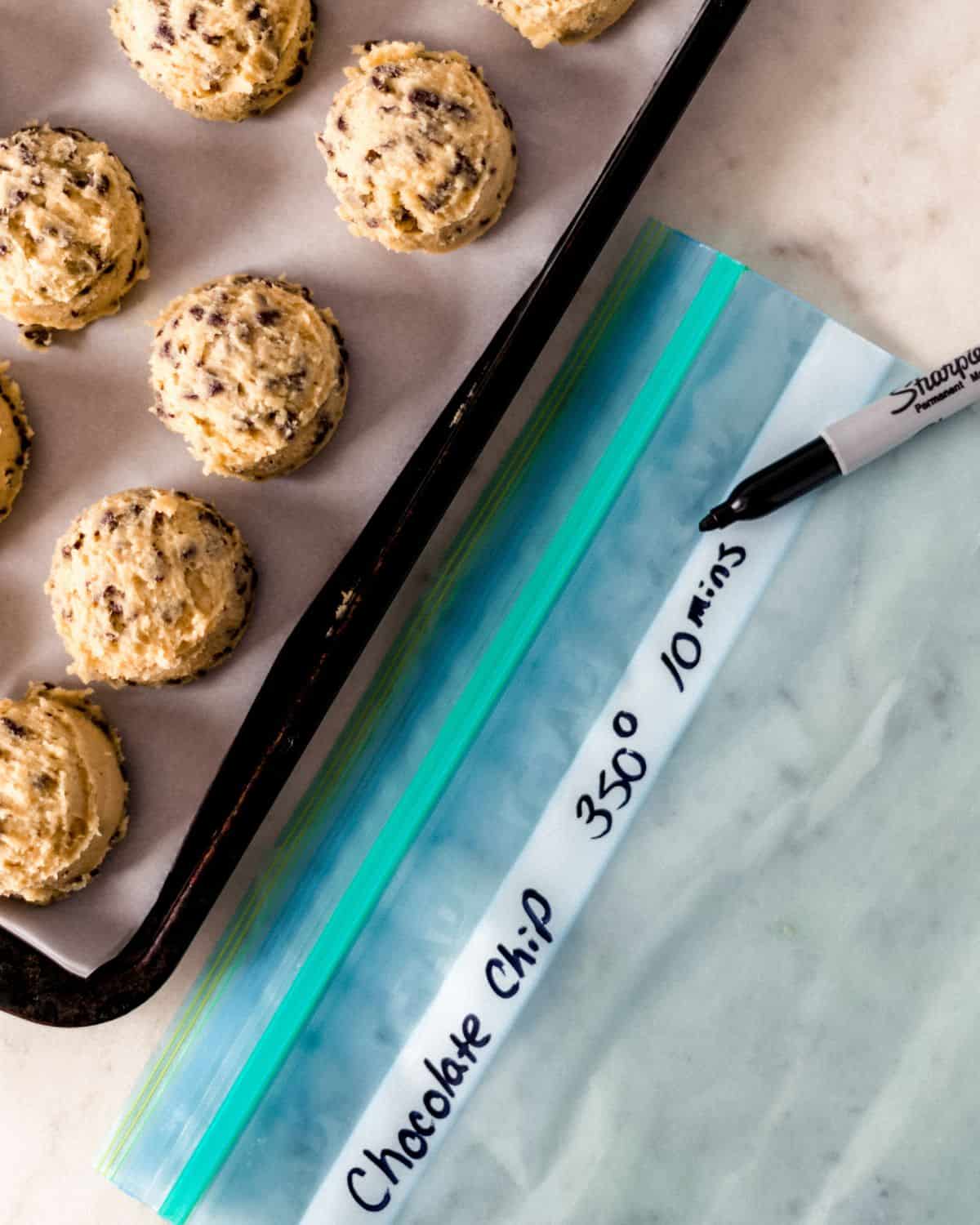 Cookie dough on parchment lined sheet pan by freezer bag and marker.
