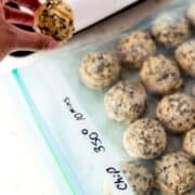 Hand holding cookie dough over freezer bag of cookies.