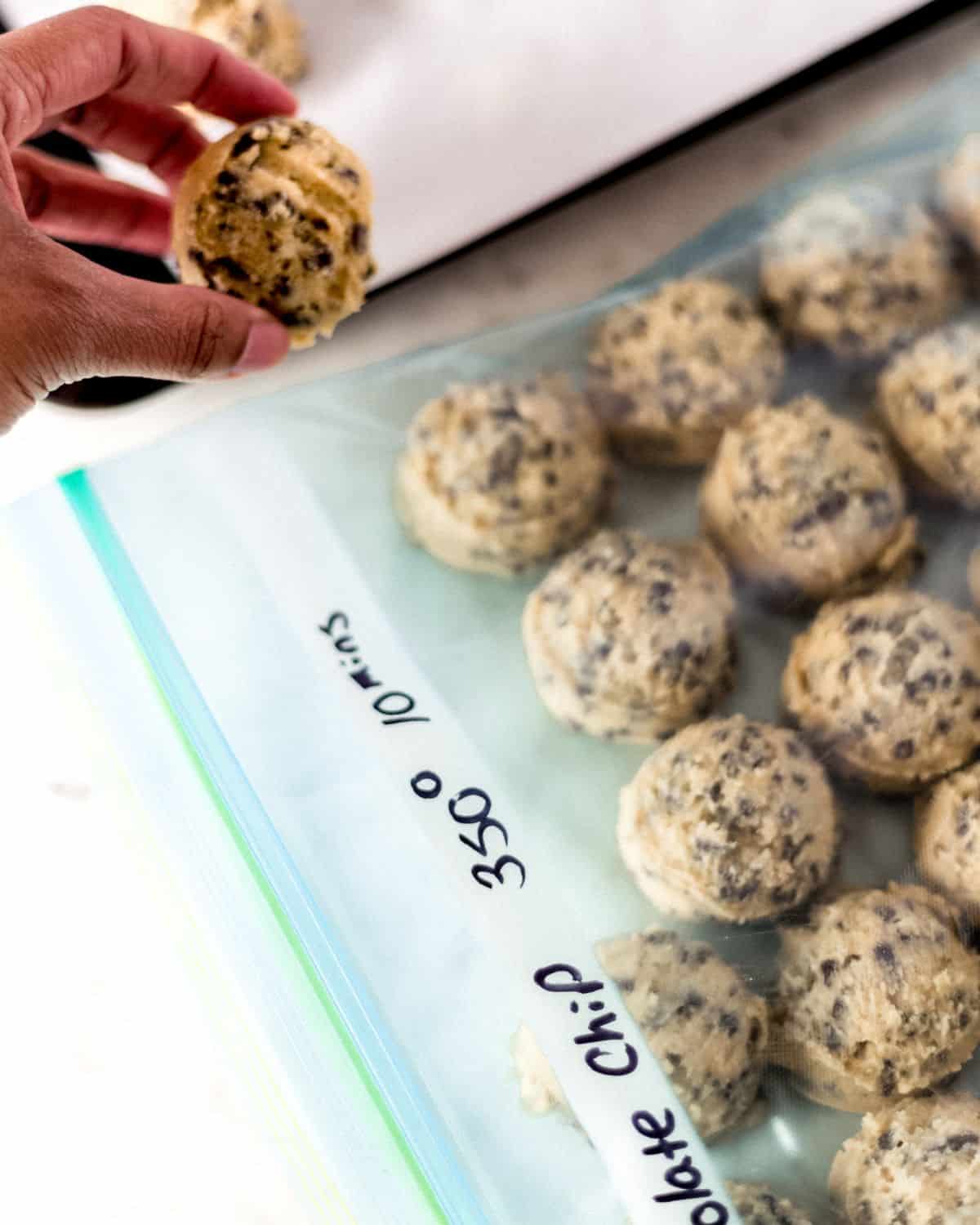 Hand holding cookie dough over freezer bag of cookies.
