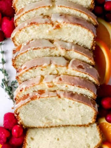 Close up view of sliced cake with fruit and herbs around it.