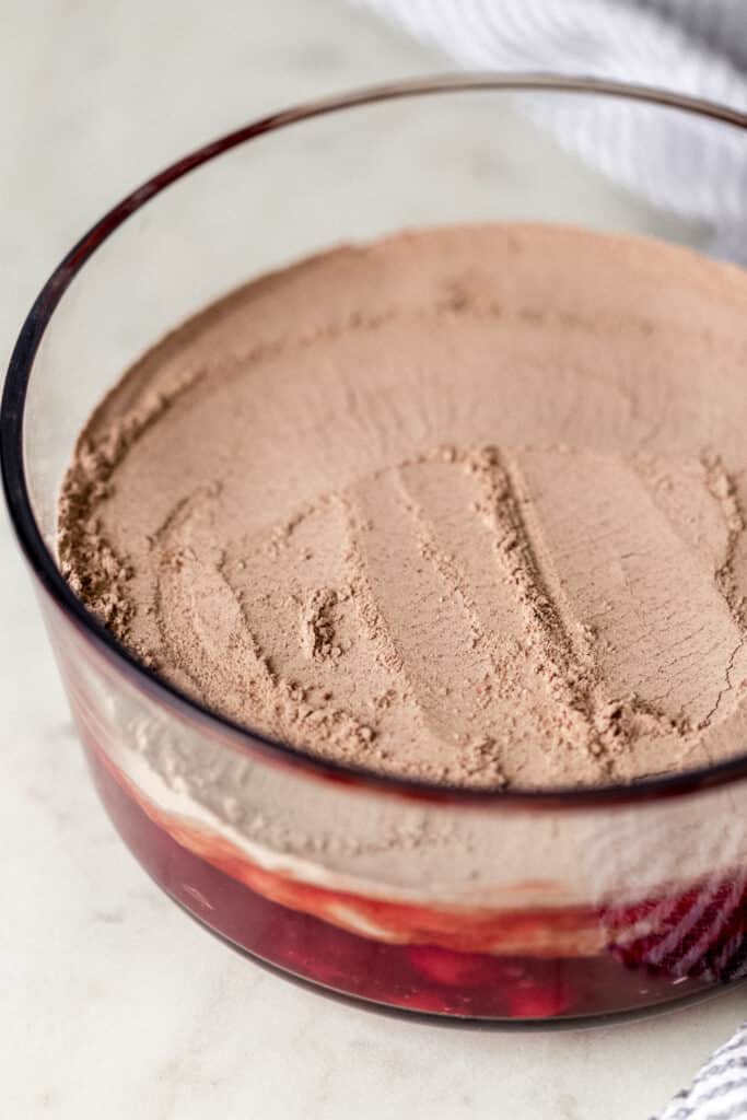 chocolate cake mix spread over cherry pie filling in glass dish for chocolate dump cake