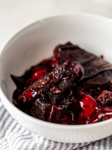 side view chocolate cherry dump cake serving in white bowl with napkin