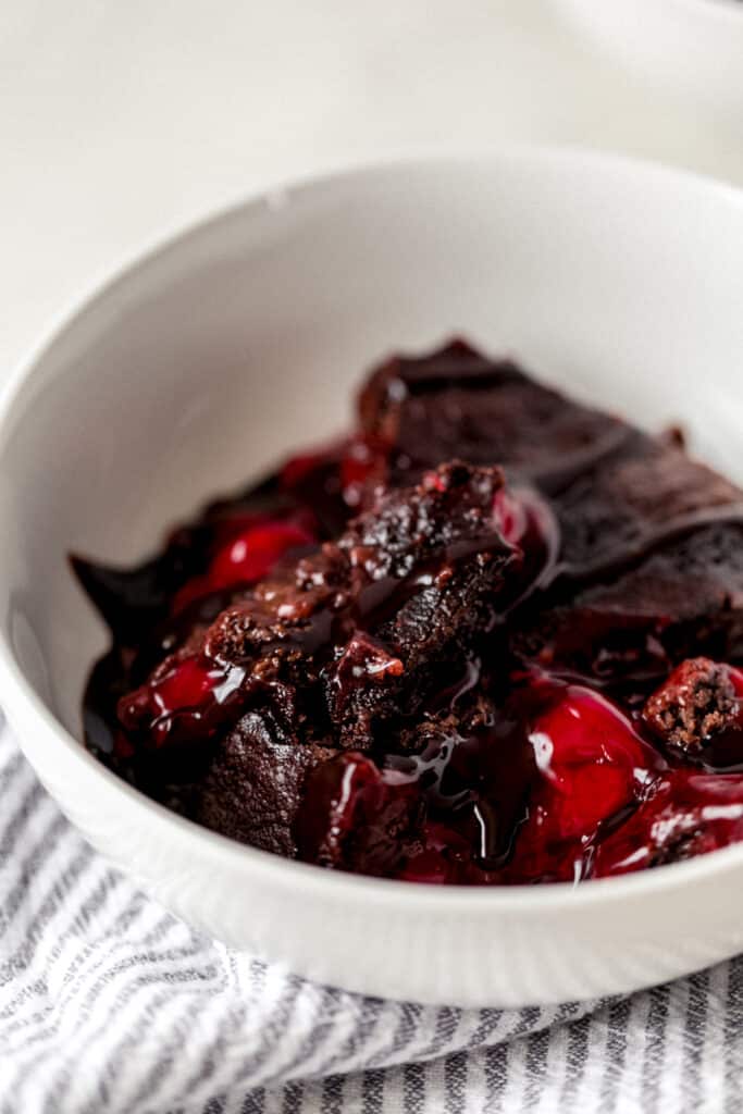 side view chocolate cherry dump cake serving in white bowl with napkin