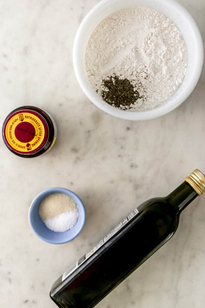 ingredients to make pizza dough in separate containers on marble surface 