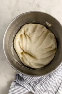 overhead view pizza dough in mixer bowl with air pressed out of it.