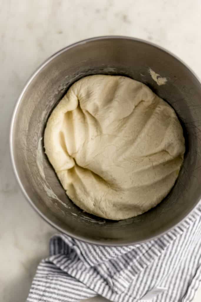 overhead view pizza dough in mixer bowl with air pressed out of it. 