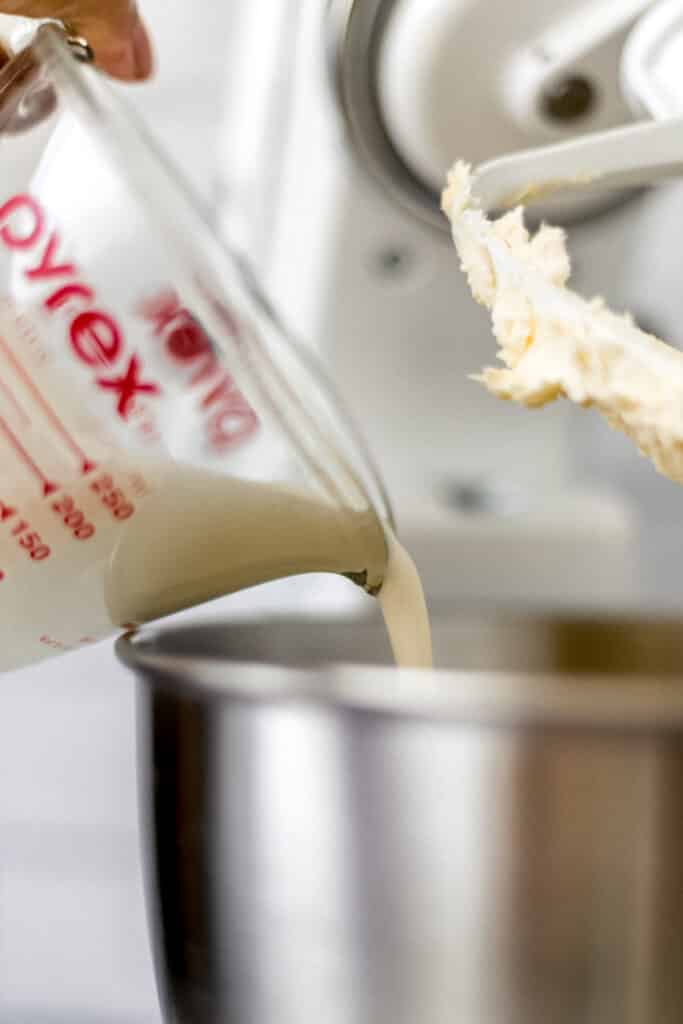 close up side view of heavy cream being poured into stand mixer bowl