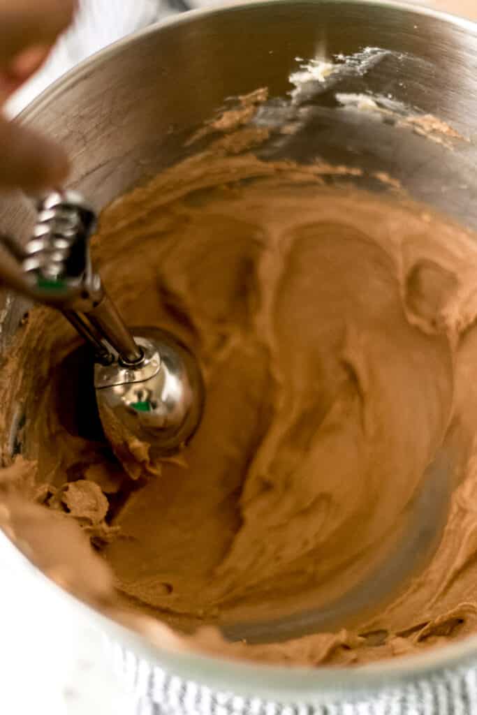 hand holding cookie scoop to in mixing bowl with keto chocolate fat bomb mixture