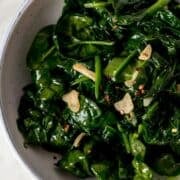 Close up view of finished spinach in a white bowl.