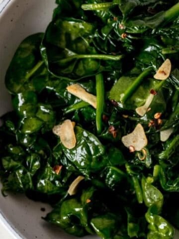 Close up view of finished spinach in a white bowl.