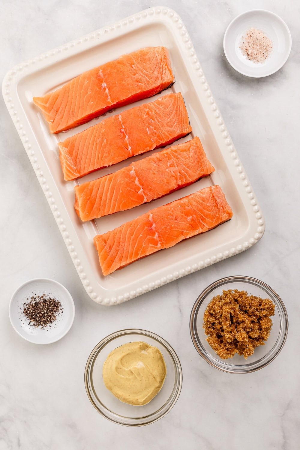 Overhead view of ingredients needed to make salmon in separate bowls on marble surface.