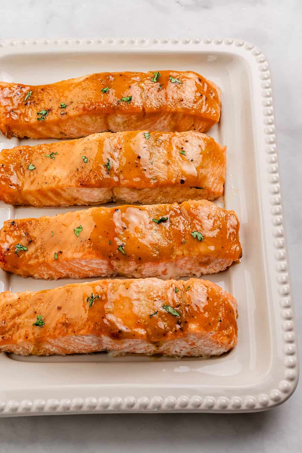 Close up view of finished salmon on white platter topped with parsley.