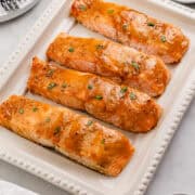 Close up view of salmon fillets on white platter surrounded by other props.