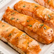 Close up view of finished salmon on white platter topped with chopped parsley.