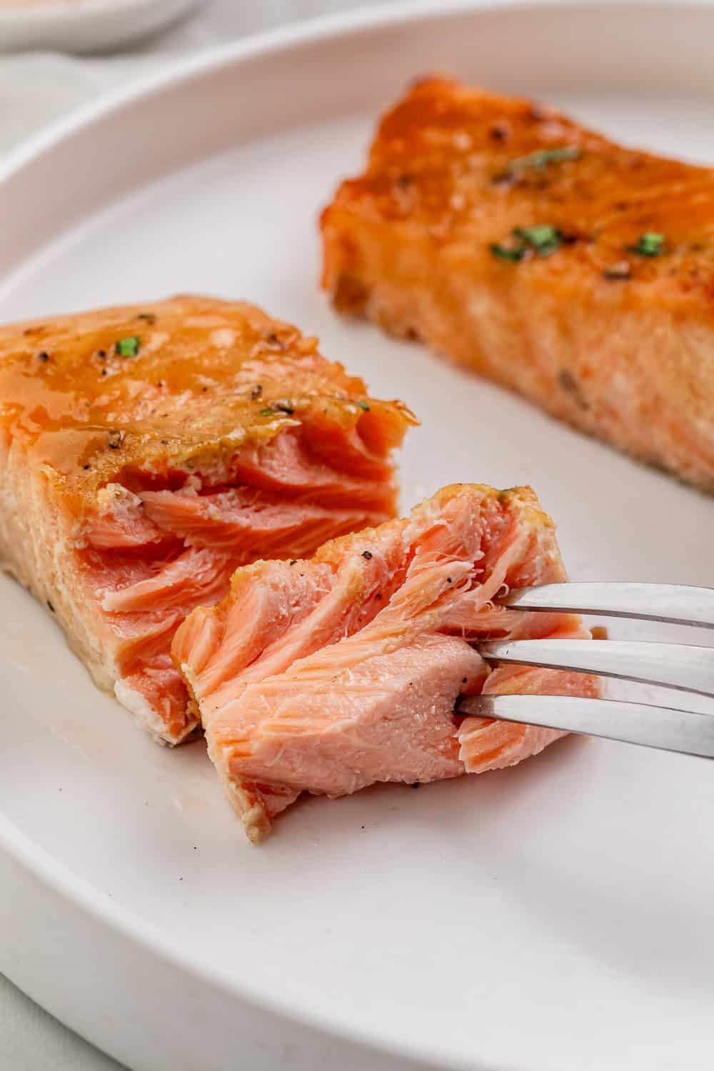 Close up view of salmon on a white plate with a fork in it.