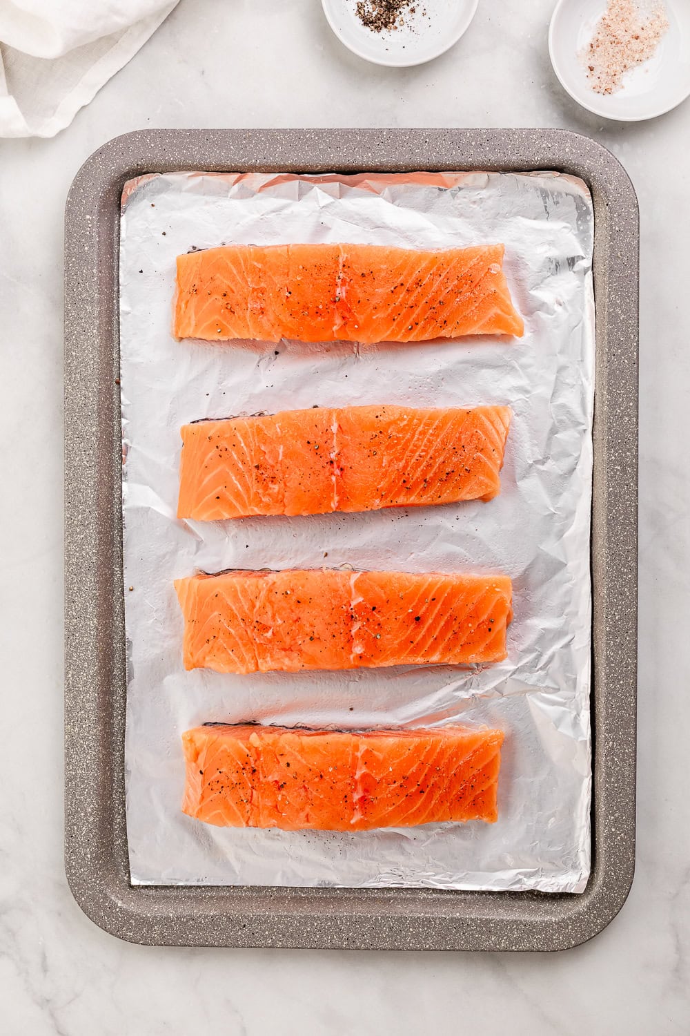 Overhead view of seasoned salmon on foil lined baking sheet.