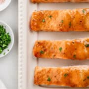 Overhead view of salmon on white platter by small bowls of salt and parsley.