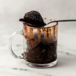 close up side view of glass mug with brownie in it with a spoonful of it over the top