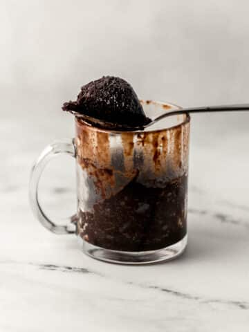 close up side view of glass mug with brownie in it with a spoonful of it over the top