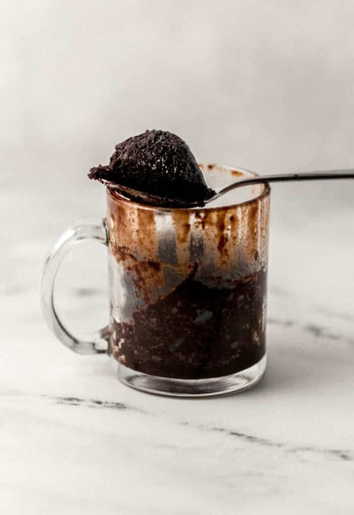 close up side view of glass mug with brownie in it with a spoonful of it over the top