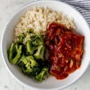 Overhead view of white bowl of pork chops, rice, and broccoli.