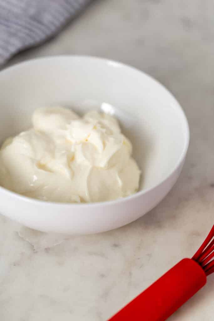 mayo in white bowl next to red whisk and napkin