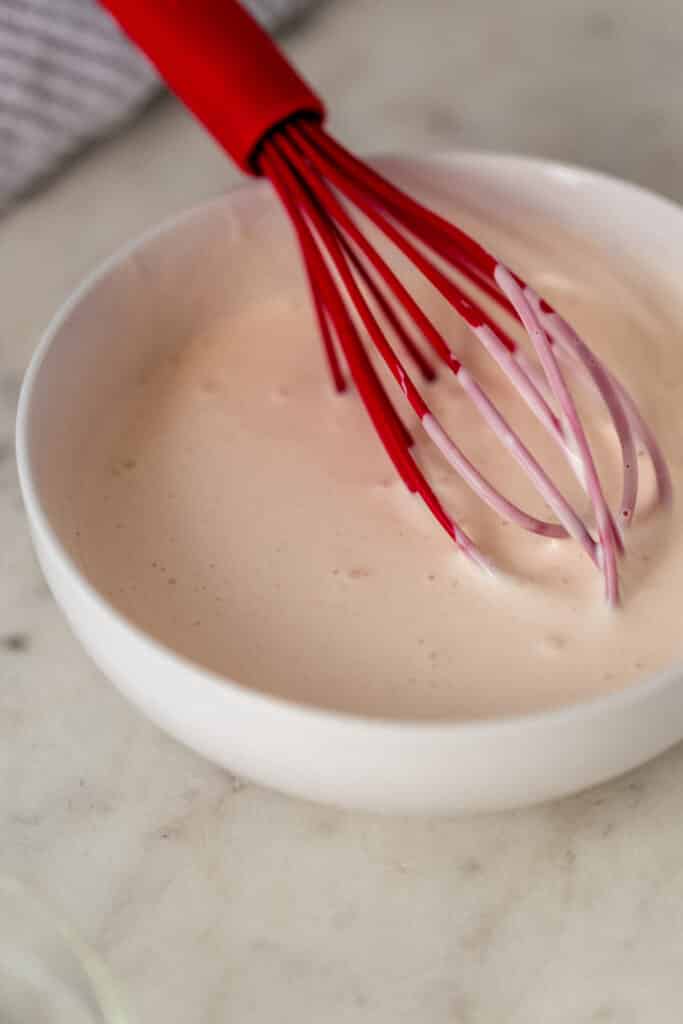 ingredients for yum yum sauce in white bowl with red whisk