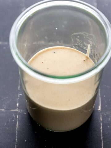 Close up side view of sauce in jar on black tile surface.