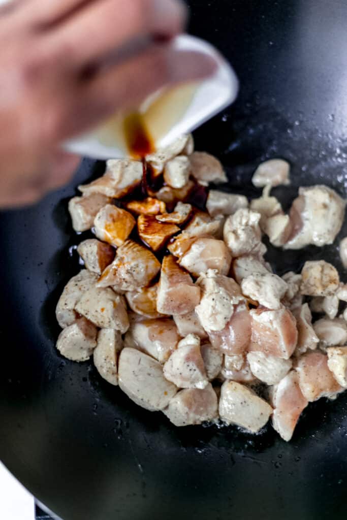 hand pouring soy sauce into wok over chicken 