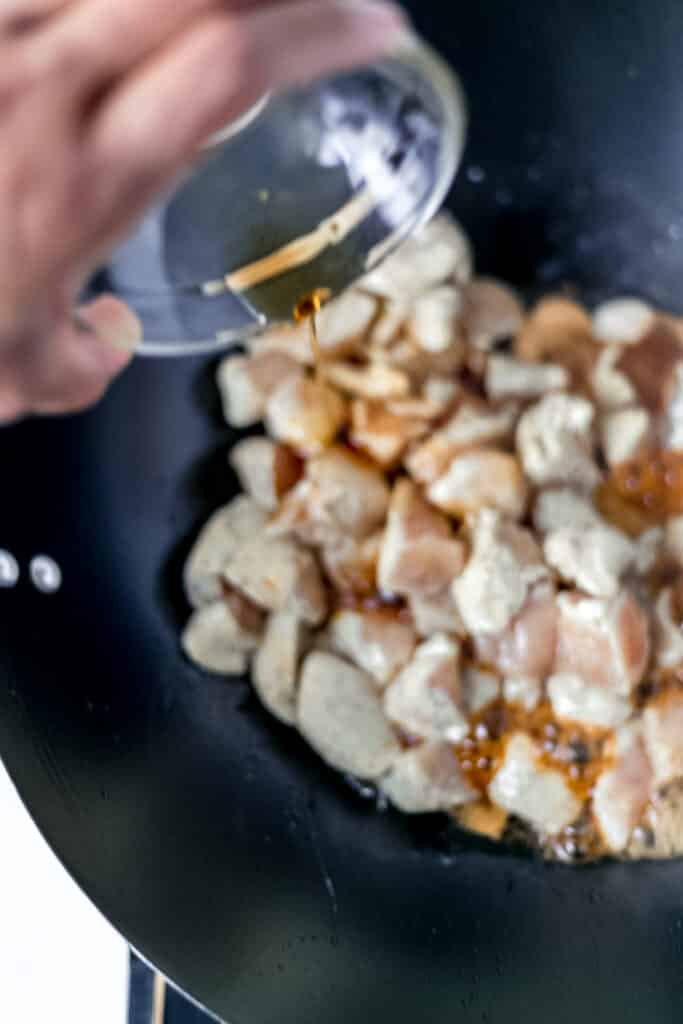 hand pouring seasame oil into wok over chicken 