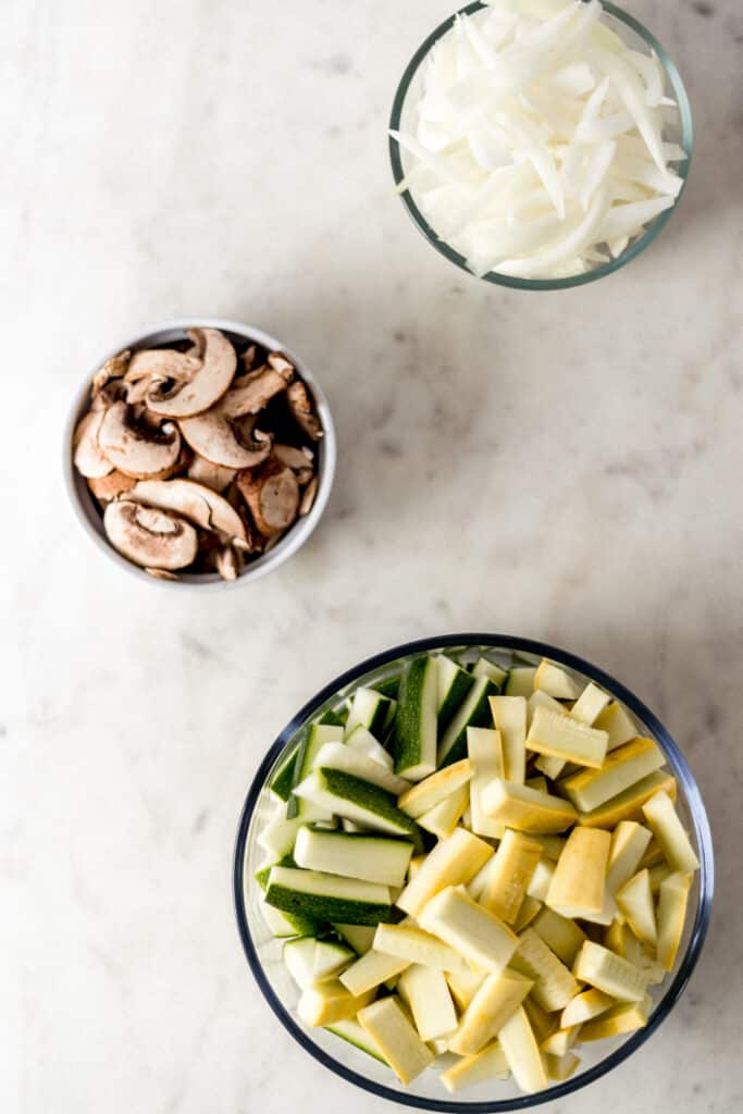 chopped onion, zucchini, and mushrooms in glass bowls