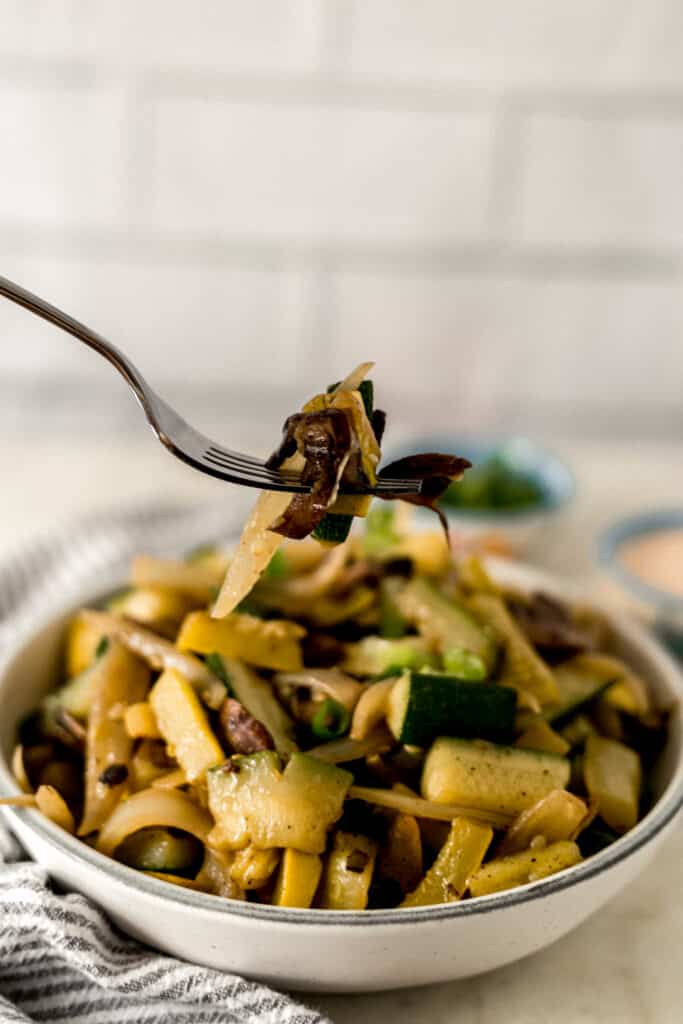 cooked vegetables in large white bowl with hand holding fork over it
