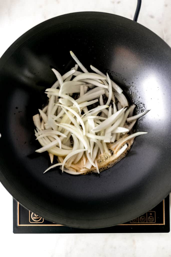 sliced onion in a wok with cooking oil and butter