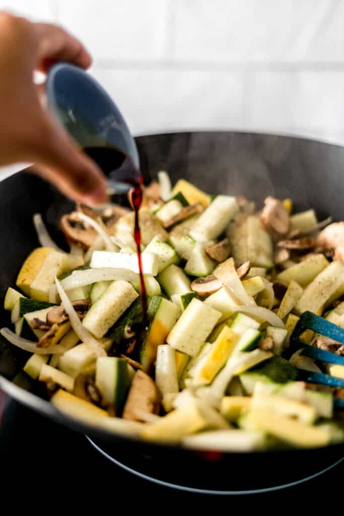 hand adding soy sauce into a wok with hibachi vegetables