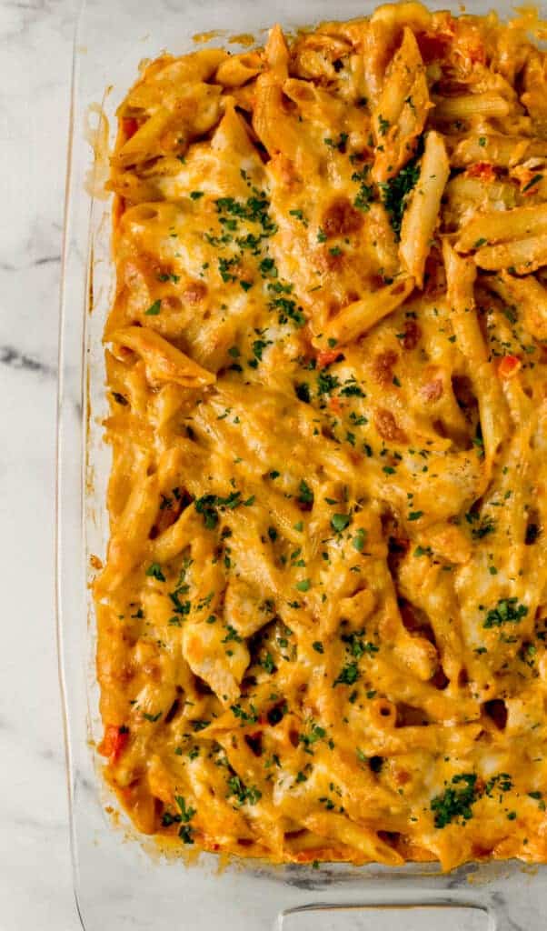 overhead view of finished enchilada pasta in glass baking dish topped with fresh chopped parsley