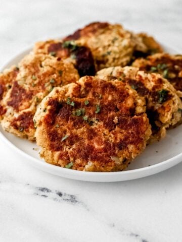 Finished salmon patties on white plate on marble surface.