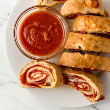 finished pepperoni bread recipe on large white plate with small glass bowl of dipping sauce