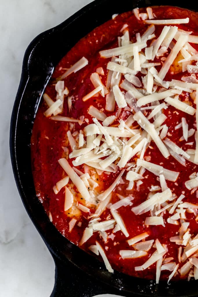 chicken in cast iron skillet topped with pasta sauce and parmesan cheese