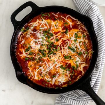 overhead view chicken mozzarella in cast iron skillet with napkin, plates, and serving spoon