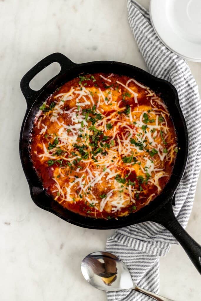 overhead view chicken mozzarella in cast iron skillet with napkin, plates, and serving spoon