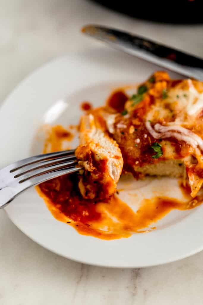 piece of finished chicken mozzarella on white plate with fork and knife 