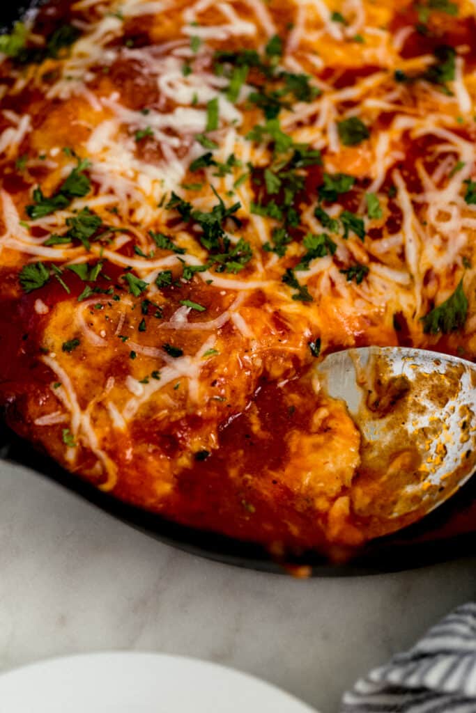 close up side view chicken mozzarella in cast iron skillet with serving spoon