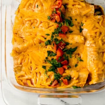 overhead view of finished enchiladas in glass baking dish topped with chopped spinach and diced tomato