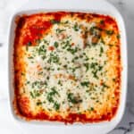 Overhead view of finished chicken mozzarella in white baking dish topped with parsley.